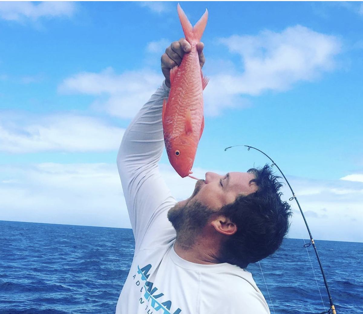 A Makai Adventures crew member kissing a red fish he just caught