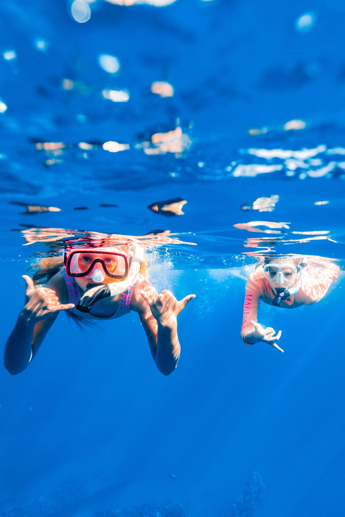 Two snorkelers in masks waving underwater in clear blue water